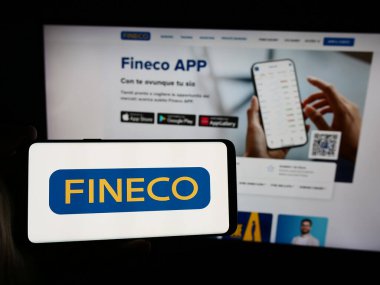 Stuttgart, Almanya - 08-12-2024: İtalyan finans hizmetleri şirketi FinecoBank S.P.A. 'nın logosuna sahip akıllı telefon sahibi kişi web sitesi önünde. Telefon ekranına odaklan.