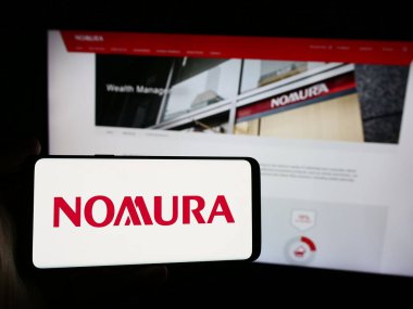 Stuttgart, Almanya - 08-12-2024: Japon finans hizmetleri şirketi Nomura Holding Inc. 'nin logosuna sahip akıllı telefon sahibi kişi web sitesi önünde. Telefon ekranına odaklan.