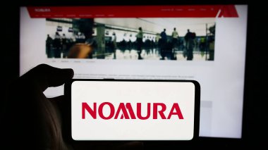 Stuttgart, Almanya - 08-12-2024: Japon finans hizmetleri şirketi Nomura Holding Inc. 'nin logosuyla cep telefonu tutan kişi web sayfasının önünde. Telefon ekranına odaklan.