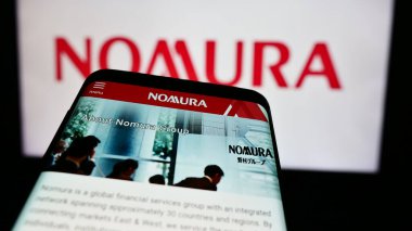 Stuttgart, Almanya - 08-12-2024: Japon finans hizmetleri şirketi Nomura Holding Inc. 'nin internet sayfası ile birlikte logo önünde cep telefonu. Telefon ekranının sol üst kısmına odaklan.