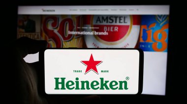 Stuttgart, Almanya - 08-12-2024: Hollandalı bira şirketi Heineken N.V. 'nin logosuyla cep telefonu tutan kişi iş sayfasının önünde. Telefon ekranına odaklan.