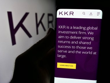 Stuttgart, Almanya - 08-13-2024: ABD 'li yatırım şirketi KKR Co. Inc.' nin web sayfası ile akıllı telefon sahibi kişi iş logosu önünde. Telefon ekranının merkezine odaklan.