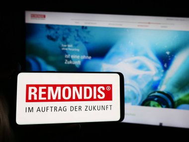 Stuttgart, Almanya - 07-31-2024: Alman atık yönetim şirketi Remondis SE Co. KG 'nin logosuna sahip akıllı telefon sahibi kişi web sitesinin önünde. Telefon ekranına odaklan.