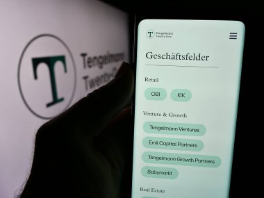 Stuttgart, Almanya - 07-31-2024: Alman holding şirketi Tengelmann 21 KG 'nin web sitesi ile logo önünde cep telefonu tutan kişi. Telefon ekranının merkezine odaklan.