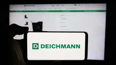 Stuttgart, Almanya - 08-01-2024: Üzerinde Alman ayakkabı perakende şirketi Deichmann SE 'nin logosu bulunan cep telefonu sahibi kişi iş sayfasının önünde. Telefon ekranına odaklan.