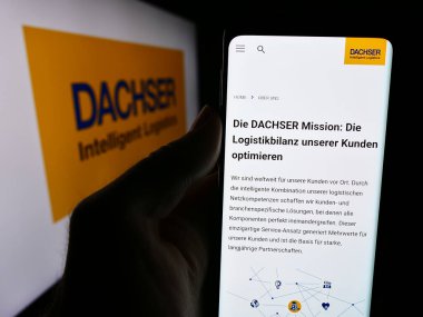 Stuttgart, Germany - 08-01-2024: Person holding mobile phone with website of German logistics company Dachser Group SE Co. KG in front of logo. Focus on center of phone display. clipart