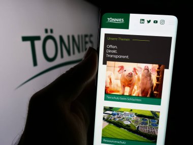 Stuttgart, Germany - 08-01-2024: Person holding mobile phone with logo of German company Toennies in front of web page. Focus on phone display. clipart