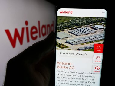 Stuttgart, Almanya - 08-01-2024: Alman metal işleme şirketi Wieland-Werke AG 'nin internet sayfası ile logo önünde cep telefonu tutan kişi. Telefon ekranının merkezine odaklan.