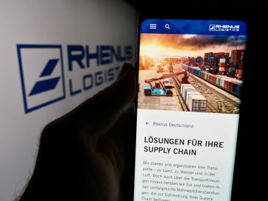 Stuttgart, Almanya - 08-01-2024: Alman lojistik şirketi Rhenus SE Co. KG 'nin internet sayfası ile cep telefonu tutan kişi iş logosu önünde. Telefon ekranının merkezine odaklan.