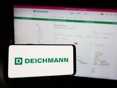 Stuttgart, Almanya - 08-01-2024: Üzerinde Alman ayakkabı perakende şirketi Deichmann SE 'nin logosu bulunan cep telefonu sahibi kişi iş sayfasının önünde. Telefon ekranına odaklan.