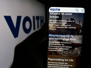 Stuttgart, Almanya - 08-02-2024: Alman teknoloji şirketi Voith GmbH Co. KGaA 'nın logo önündeki web sayfası ile cep telefonu tutan kişi. Telefon ekranının merkezine odaklan.