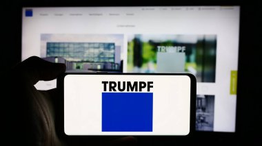 Stuttgart, Almanya - 08-02-2024: Alman mühendislik şirketi TRUMPF SE Co. KG 'nin logosuyla cep telefonu tutan kişi iş sayfasının önünde. Telefon ekranına odaklan.