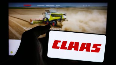 Stuttgart, Almanya - 08-02-2024: Alman tarım makineleri şirketi Claas KGaA mbH 'nin logosuna sahip cep telefonu sahibi kişi web sayfasının önünde. Telefon ekranına odaklan.