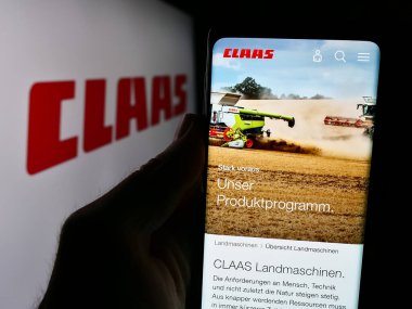 Stuttgart, Almanya - 08-02-2024: Alman tarım makineleri şirketi Claas KGaA mbH 'nin web sayfası ile logo önünde cep telefonu tutan kişi. Telefon ekranının merkezine odaklan.