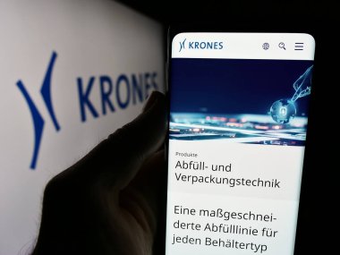 Stuttgart, Almanya - 08-05-2024: Alman mühendislik şirketi Krones AG 'nin web sayfası ile birlikte iş logosu önünde cep telefonu tutan kişi. Telefon ekranının merkezine odaklan.