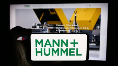 Stuttgart, Almanya - 08-05-2024: Alman şirketi Mann Hummel International GmbH Co. KG 'nin logosuyla cep telefonu tutan kişi iş sayfasının önünde. Telefon ekranına odaklan.