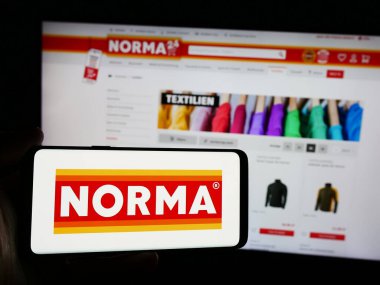 Stuttgart, Almanya - 08-05-2024: Sitenin önünde Norma Lebensmittelfilialbetrieb Co. KG şirketinin logosuna sahip kişi. Telefon ekranına odaklan.