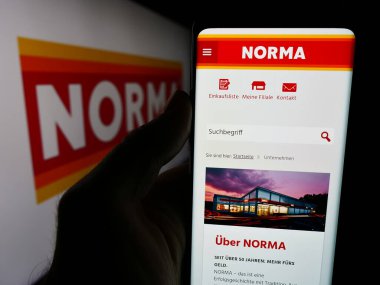 Stuttgart, Almanya - 08-05-2024: Logolu Norma Lebensmittelfilialbetrieb Stiftung Co. KG şirketinin internet sitesiyle cep telefonu bulunduran kişi. Telefon ekranının merkezine odaklan.