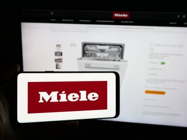 Stuttgart, Almanya - 08-05-2024: Alman ev aletleri şirketi Miele Cie 'nin logosuna sahip akıllı telefon sahibi kişi. KG web sitesinin önünde. Telefon ekranına odaklan.