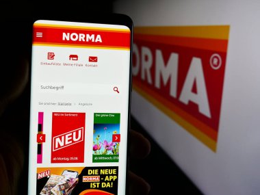 Stuttgart, Almanya - 08-05-2024: Logolu Norma Lebensmittelfilialbetrieb Stiftung Co. KG şirketinin web sayfası ile cep telefonu tutan kişi. Telefon ekranının merkezine odaklan.