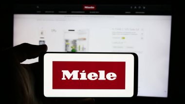 Stuttgart, Almanya - 08-05-2024: Alman ev aletleri şirketi Miele Cie 'nin logosuyla cep telefonu tutan kişi. KG iş sayfasının önünde. Telefon ekranına odaklan.