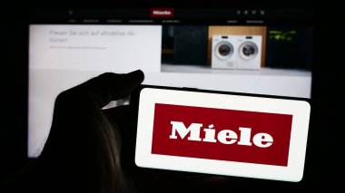 Stuttgart, Almanya - 08-05-2024: Alman ev aletleri şirketi Miele Cie 'nin logosuna sahip cep telefonu sahibi kişi. KG iş sayfasının önünde. Telefon ekranına odaklan.