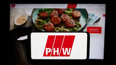 Stuttgart, Almanya - 08-05-2024: İnternet sayfası önünde Alman et işleme şirketi Lohmann Co. AG 'nin (PHW-Gruppe) logosuyla cep telefonu tutan kişi. Telefon ekranına odaklan.