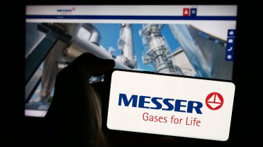 Stuttgart, Germany - 08-05-2024: Person holding mobile phone with logo of German industrial gases company Messer SE Co. KGaA in front of business web page. Focus on phone display. clipart