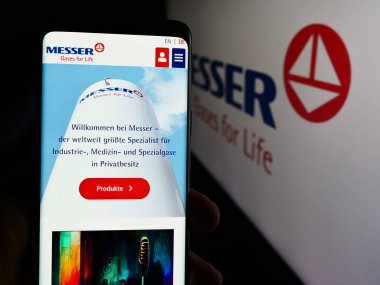 Stuttgart, Germany - 08-05-2024: Person holding cellphone with webpage of German industrial gases company Messer SE Co. KGaA in front of logo. Focus on center of phone display. clipart