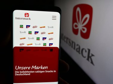 Stuttgart, Almanya - 08-05-2024: Alman aperatif yiyecek şirketi Intersnack Group GmbH Co. KG 'nin logolu web sayfası ile akıllı telefon tutan kişi. Telefon ekranının merkezine odaklan.