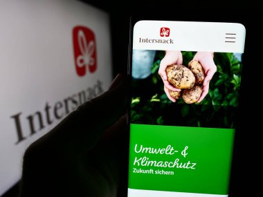 Stuttgart, Almanya - 08-05-2024: Alman aperatif yiyecek şirketi Intersnack Group GmbH Co. KG 'nin logolu web sayfası ile akıllı telefon tutan kişi. Telefon ekranının merkezine odaklan.