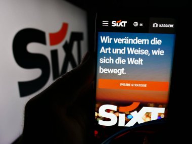 Stuttgart, Almanya - 08-06-2024: Alman otomobil kiralama şirketi Sixt SE 'nin internet sayfası ile iş logosu önünde cep telefonu tutan kişi. Telefon ekranının merkezine odaklan.