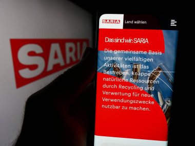 Stuttgart, Almanya - 08-06-2024: Alman gıda şirketi Saria AS GmbH Co. KG 'nin internet sayfası ile logo önünde cep telefonu tutan kişi. Telefon ekranının merkezine odaklan.