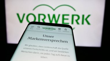 Stuttgart, Germany - 08-07-2024: Mobile phone with website of German household appliances company Vorwerk SE Co. KG in front of business logo. Focus on top-left of phone display. clipart