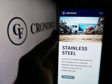 Stuttgart, Almanya - 08-07-2024: Alman metal geri dönüşüm şirketi Cronimet Holding GmbH 'nin web sitesiyle logo önünde cep telefonu tutan kişi. Telefon ekranının merkezine odaklan.