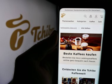 Stuttgart, Almanya - 08-07-2024: Alman kahve perakende şirketi Tchibo GmbH 'nin internet sayfası ile akıllı telefon taşıyan kişi iş logosu önünde. Telefon ekranının merkezine odaklan.