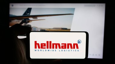 Stuttgart, Almanya - 08-07-2024: Alman şirketi Hellmann Worldwide Logistics SE Co. KG 'nin logosuyla cep telefonu tutan kişi iş sayfası önünde. Telefon ekranına odaklan.