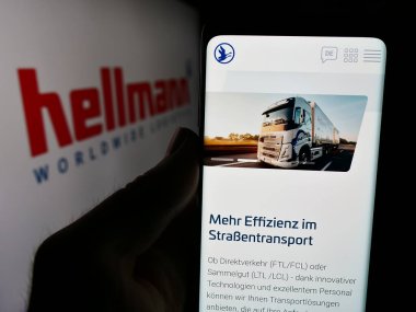 Stuttgart, Almanya - 08-07-2024: Alman şirketi Hellmann Worldwide Logistics SE Co. KG 'nin logolu web sayfası ile akıllı telefon sahibi kişi. Telefon ekranının merkezine odaklan.