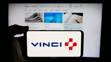 Stuttgart, Almanya - 08-07-2024: Fransız imtiyaz şirketi Vinci S.A. 'nın logosuyla cep telefonu tutan kişi iş sayfasının önünde. Telefon ekranına odaklan.
