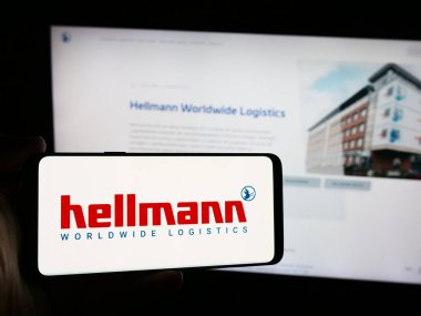 Stuttgart, Almanya - 08-07-2024: Alman şirketi Hellmann Worldwide Logistics SE Co. KG 'nin logosuna sahip akıllı telefon sahibi kişi web sitesi önünde. Telefon ekranına odaklan.
