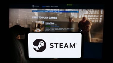 Stuttgart, Germany - 08-08-2024: Person holding cellphone with logo of US video game distribution company Steam (Valve) in front of business webpage. Focus on phone display. clipart