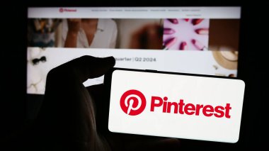 Stuttgart, Almanya - 08-09-2024: Amerikan sosyal medya şirketi Pinterest Inc. 'in logosuna sahip cep telefonu sahibi kişi iş sayfasının önünde. Telefon ekranına odaklan.