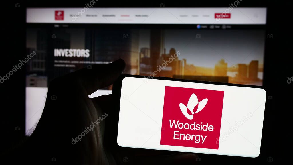 Stuttgart, Germany - 08-09-2024: Person holding mobile phone with logo of Australian company Woodside Energy Group Limited in front of business web page. Focus on phone display.