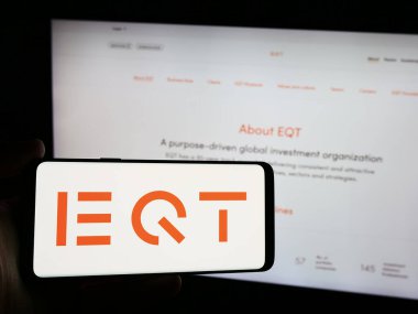 Stuttgart, Germany - 08-13-2024: Person holding smartphone with logo of Swedish investment management company EQT AB in front of website. Focus on phone display. clipart