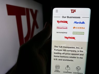 Stuttgart, Almanya - 08-13-2024: ABD 'li mağaza şirketi The TJX Companies Inc.' in logo önündeki web sayfası ile cep telefonu tutan kişi. Telefon ekranının merkezine odaklan.