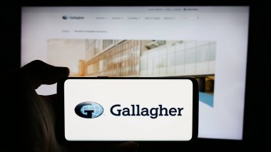Stuttgart, Almanya - 08-13-2024: ABD 'li sigorta şirketi Arthur J. Gallagher Co. (AJG)' nin logosuyla cep telefonu sahibi kişi iş sayfasının önünde. Telefon ekranına odaklan.