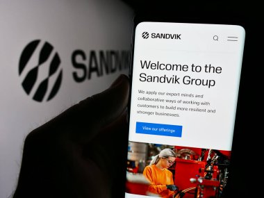 Stuttgart, Almanya - 08-15-2024: İsveçli mühendislik şirketi Sandvik AB 'nin web sayfası ile iş logosu önünde cep telefonu tutan kişi. Telefon ekranının merkezine odaklan.