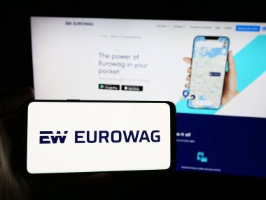 Stuttgart, Germany - 08-15-2024: Person holding smartphone with logo of Czech company W.A.G. payment solutions a.s. (Eurowag) in front of website. Focus on phone display. clipart