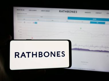 Stuttgart, Almanya - 08-16-2024: İngiliz finans şirketi Rathbones Group plc 'in logosuna sahip cep telefonu sahibi kişi iş sayfasının önünde. Telefon ekranına odaklan.