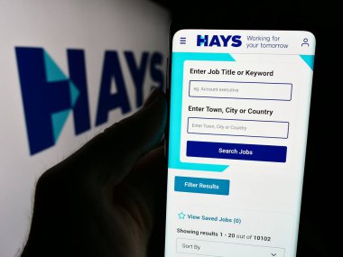 Stuttgart, Almanya - 08-16-2024: İngiliz işe alım şirketi Hays plc 'in web sayfası ile birlikte iş logosu önünde cep telefonu tutan kişi. Telefon ekranının merkezine odaklan.